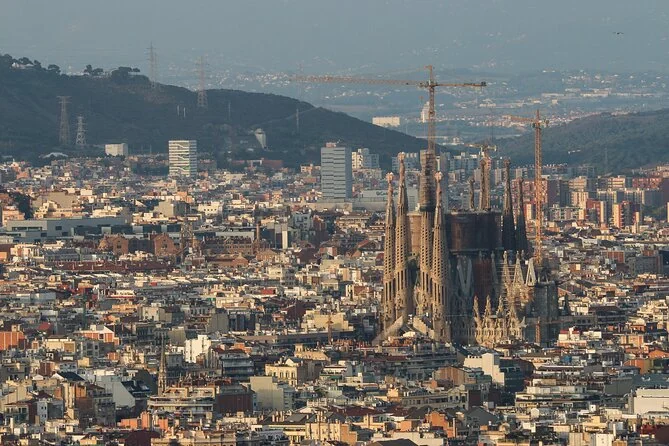 The Sagrada Familia spires rising above Barcelona's rooftops, with cranes and hills behind