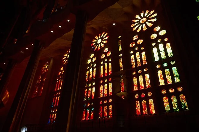 Red, orange and yellow stained-glass windows glowing in a darkened Sagrada Familia interior